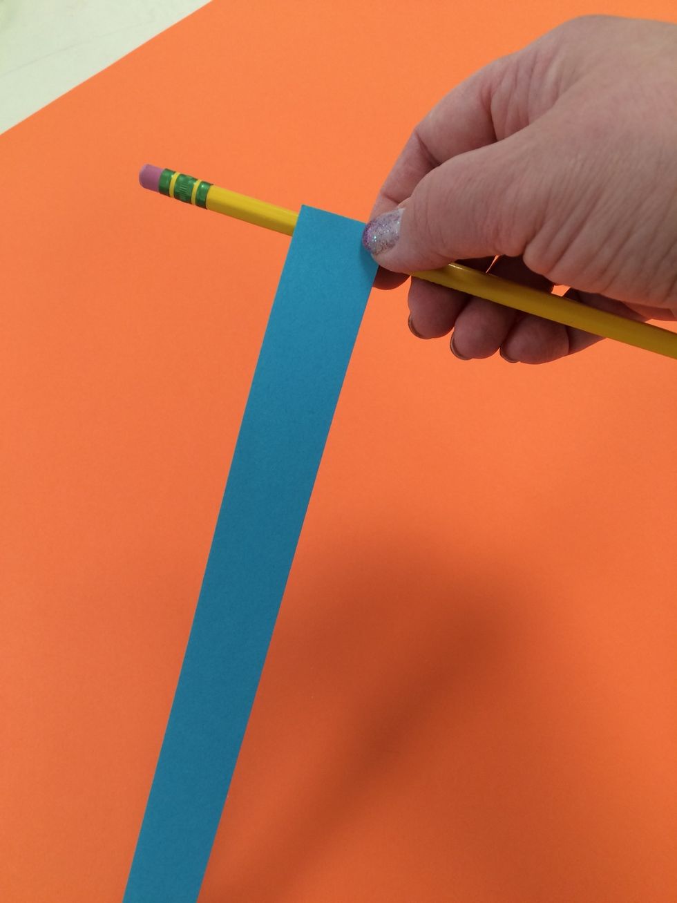 Hold one strip of paper up to a pencil or marker as shown.