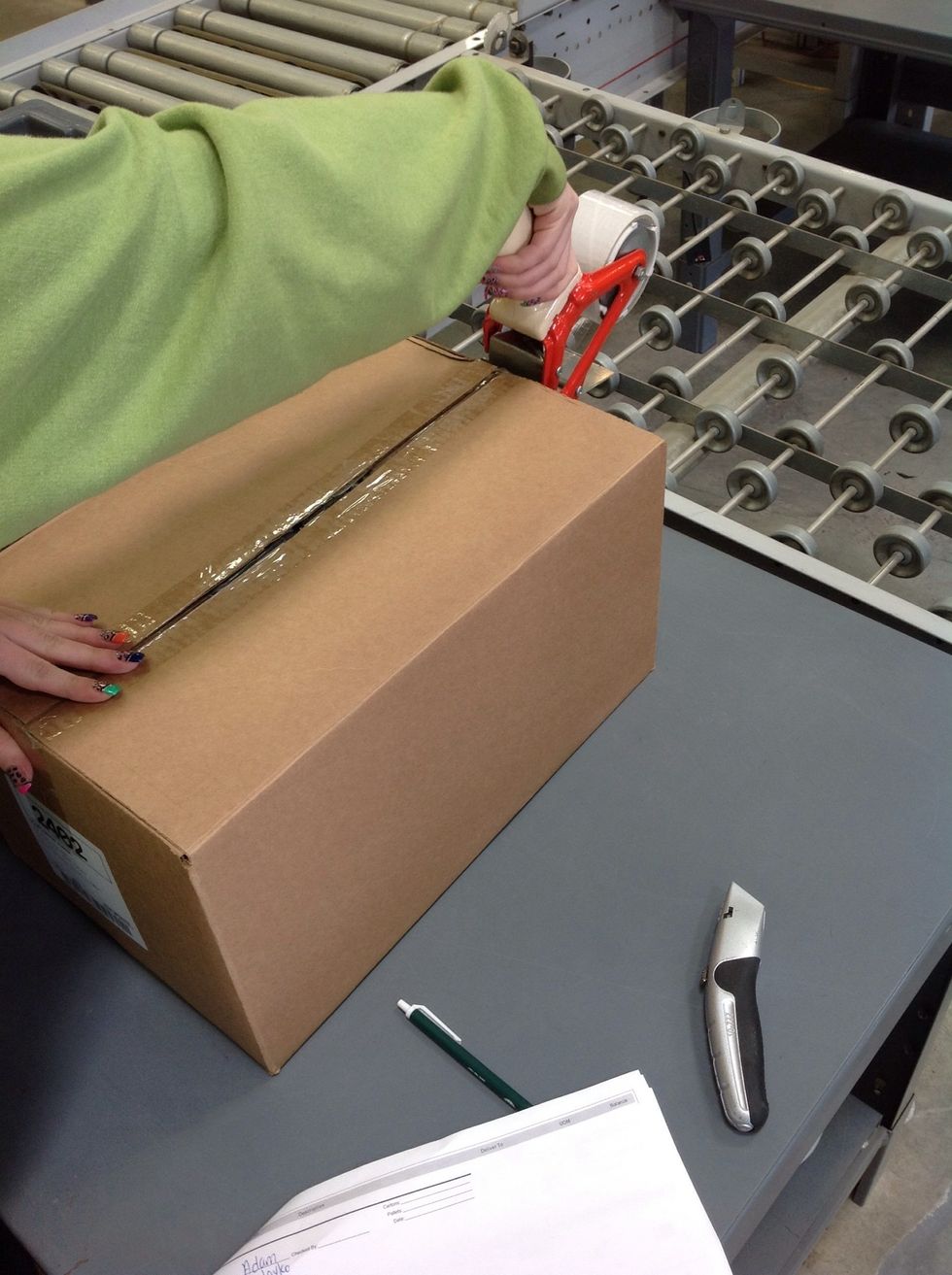 Hold the flaps closed with your left hand as you take the tape gun and secure the tape on the far end of the box.