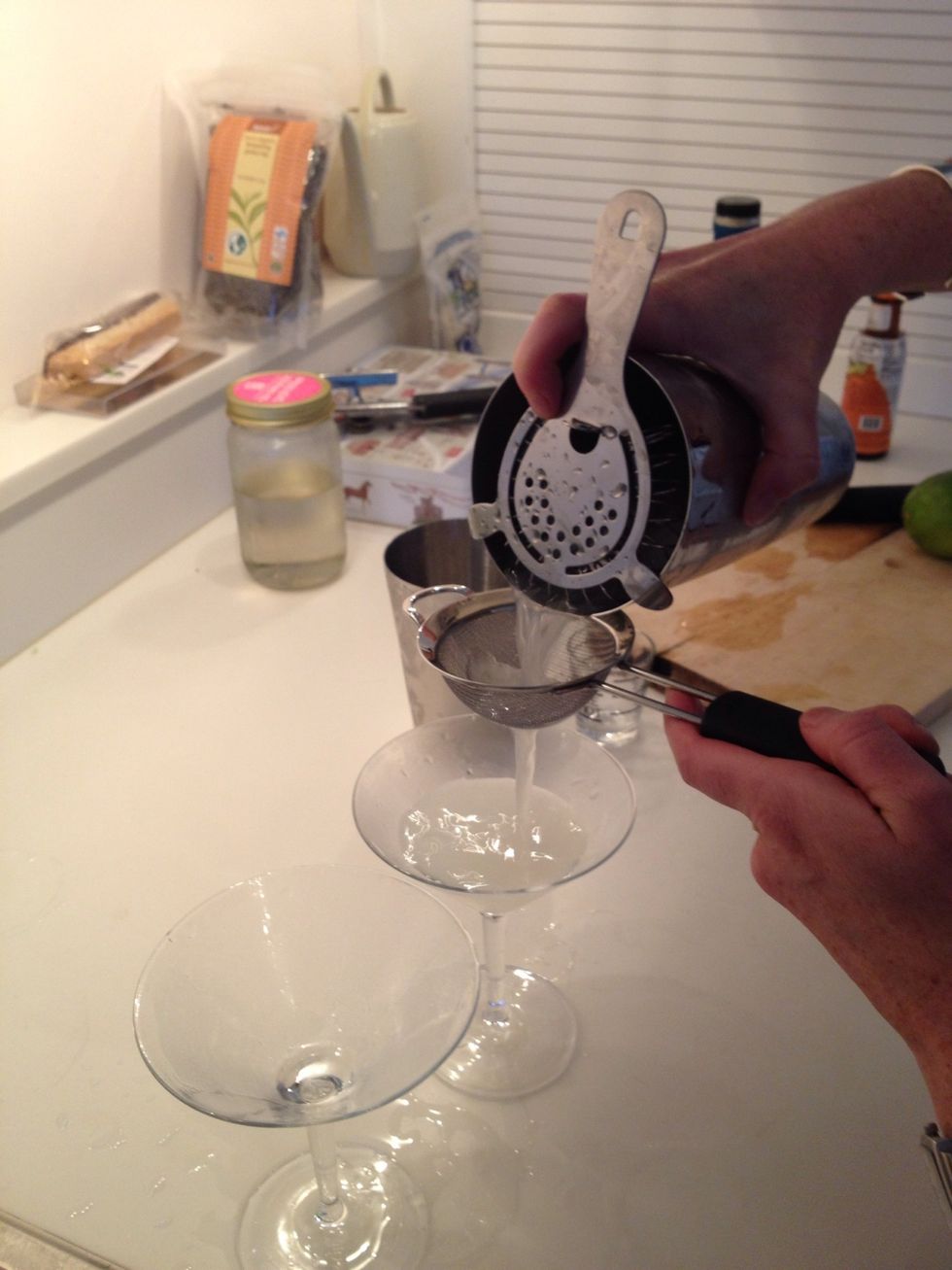 Hold the Hawthorne strainer over the shaker and pour through the tea strainer to filter any ice chips. Split the gimlet between the two glasses.
