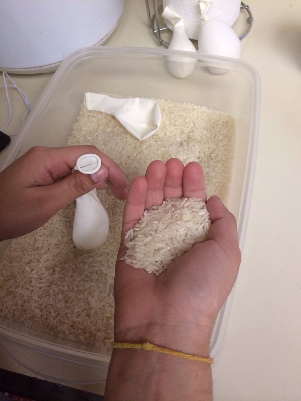 Hold your stretched-out balloon neck up. Take a handful of rice in your other hand.