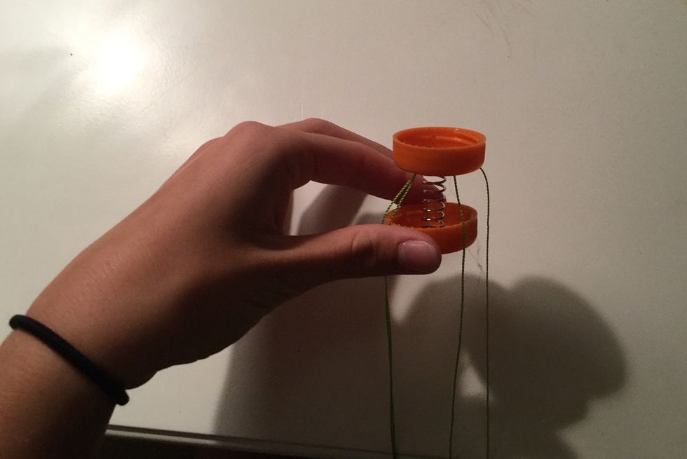 Hot glue each end of the spring and attach to each bottle cap with the threaded cap facing outward and the plain cap facing inward.