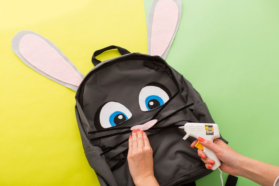 Hot glue each piece to the backpack. Then, let dry.