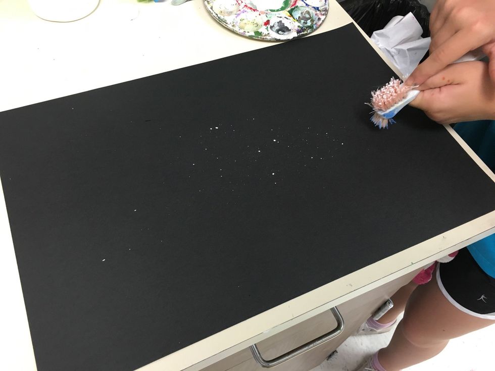 I add a little bit of water to the white paint to make it more fluid, then scrub the brush into the white paint on a plate or palette. Use your finger to pull back on the bristles splatting the paper