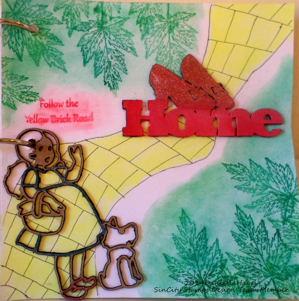 I drew the yellow brick road and colored it with yellow Pan Pastel.  I stamped the leaves with Versamark ink and colored them green.  I glued on the Dorothy shape and word.