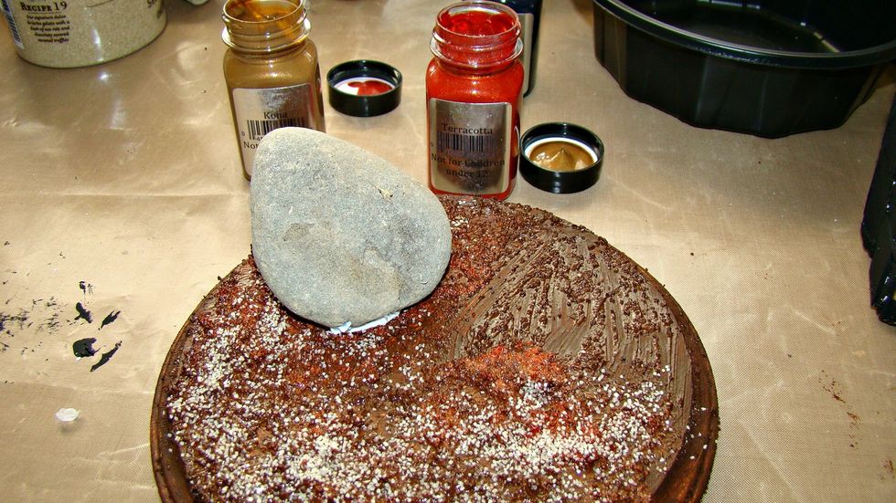 I got a rock from the outside and adhere with 3D Gel Medium to prop the coffin lid up on the base. Paint the rock black.