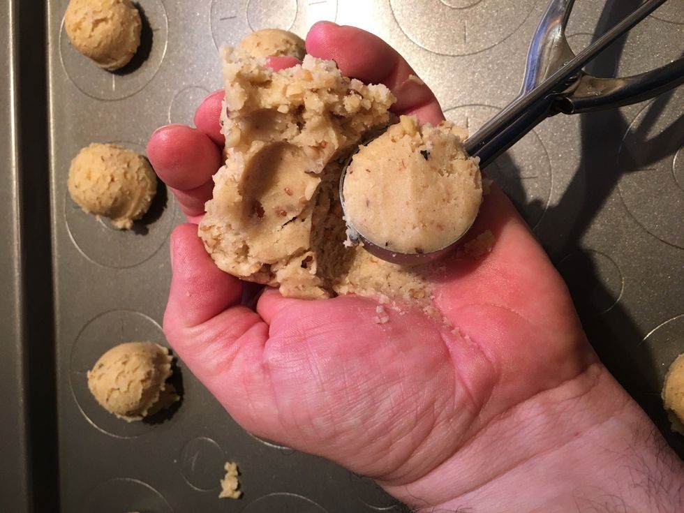 I grab a small portion of dough in my left hand, grab the cookie scooper with my right, grabbing cookie dough with the scooper and pressing it into your palm to level off the dough.
