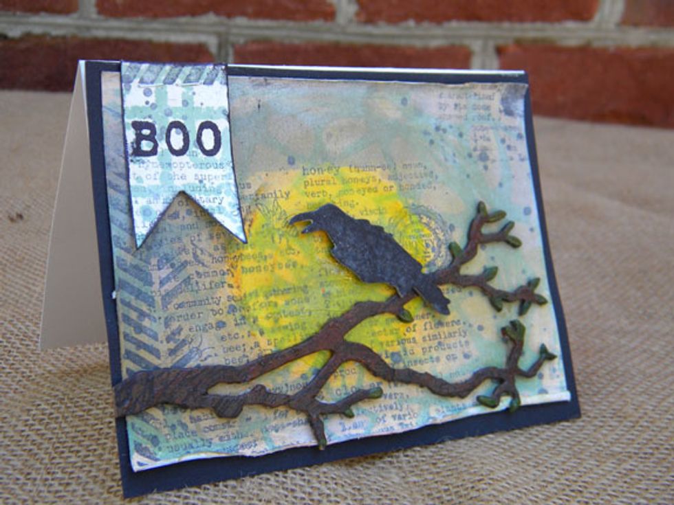 I made the branch and raven with a Tim Holtz die and chipboard, then painted them with Velvets. I also wanted to calm down the background a bit and dabbed on watered down gesso and added the moon.