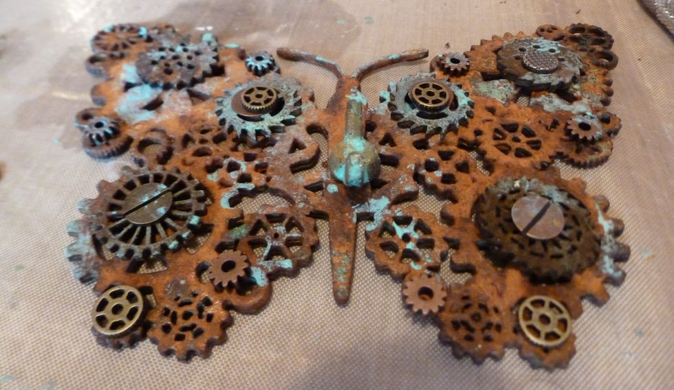 I start to add layers of the chipboard pieces and metal gears until I get an effect I like. (I added some patina to the pieces by just dabbing my finger into the paint and rubbing randomly.