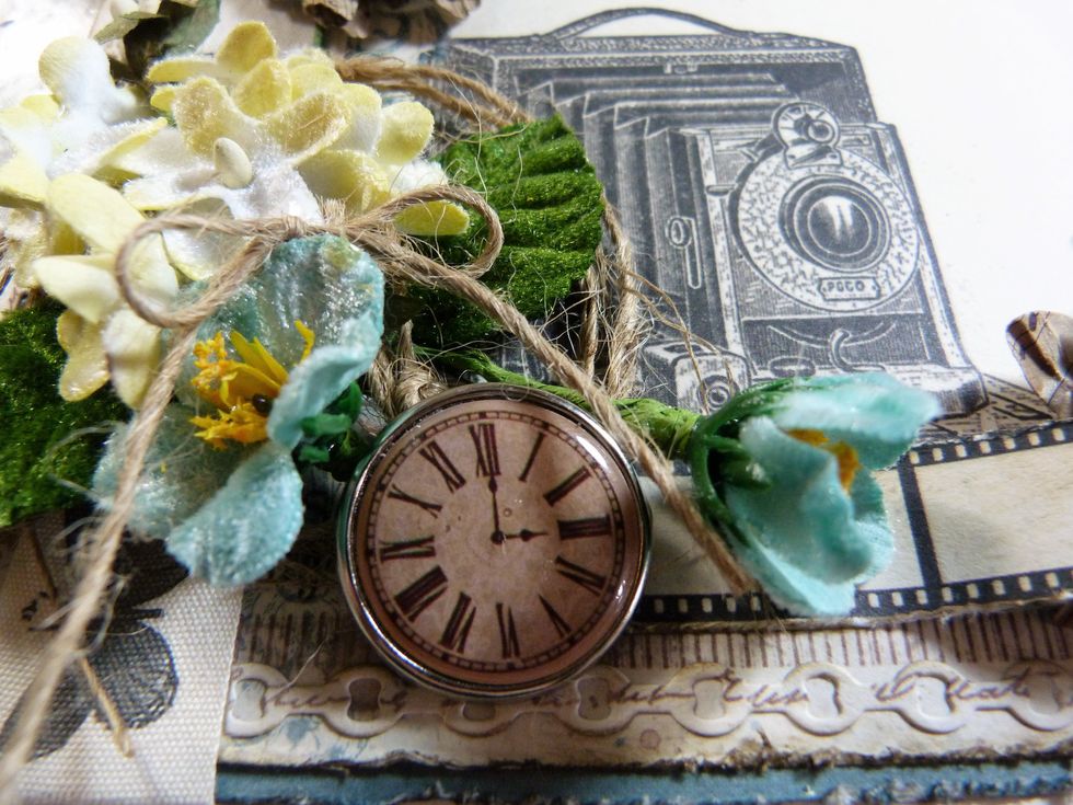 I trimmed the fasteners off of the big clock Brad & glued it into my flower cluster. I also added a string bow on top of the yellow flowers and some green leaves.