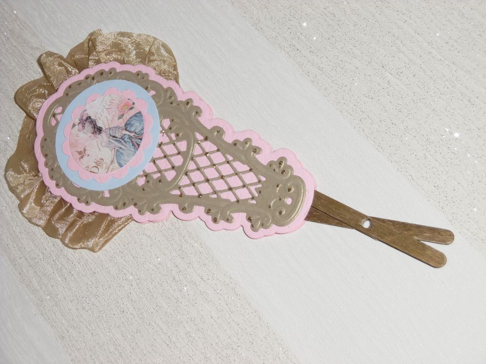 Image of Lady punched out and layered with pink and blue card as a motif for each panel. Two wooden coffee stirrers painted gold and silky crush ribbon sandwiched between the two pink layers of card.