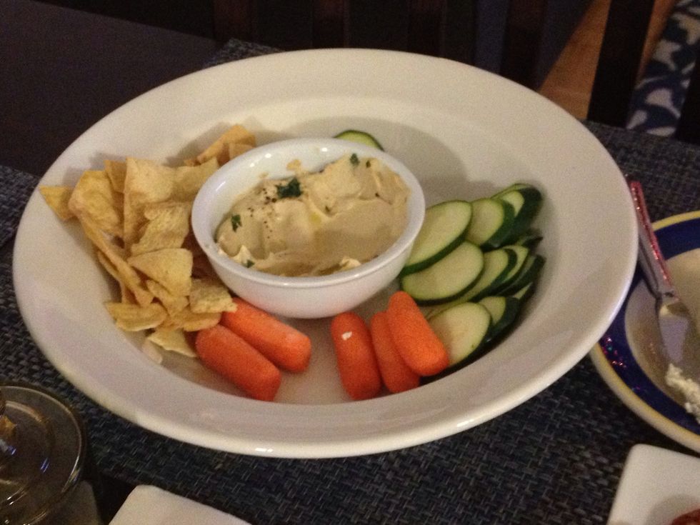 In a large serving bowl, plate sliced zucchini, baby carrots and plain pita chips. Add chopped fresh basil or parsley, black pepper and olive oil on hummus.