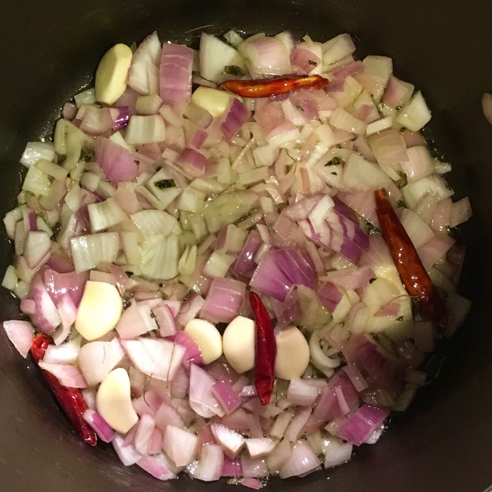 In a pot over medium heat, add oil. As the oil heats up add asafoetida, mustard seeds, dried red chilies and garlic cloves. As mustard seeds crackle, add onion and saut\u00e9 until its golden brown.