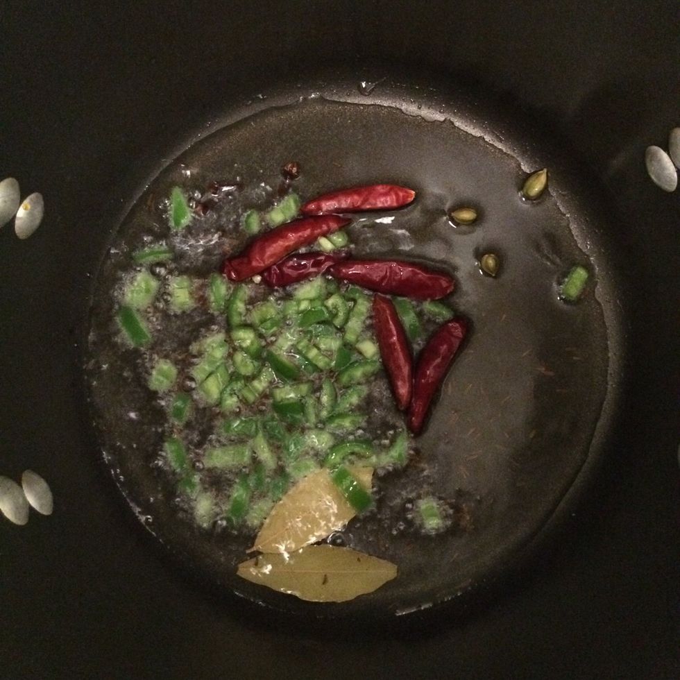 In a pot over medium heat, add oil. As the oil heats up, add cumin seeds, bay leaves, Japanese chili pods, cloves and green cardamom pods. In about 2 mins. add the chopped serrano chili pepper.