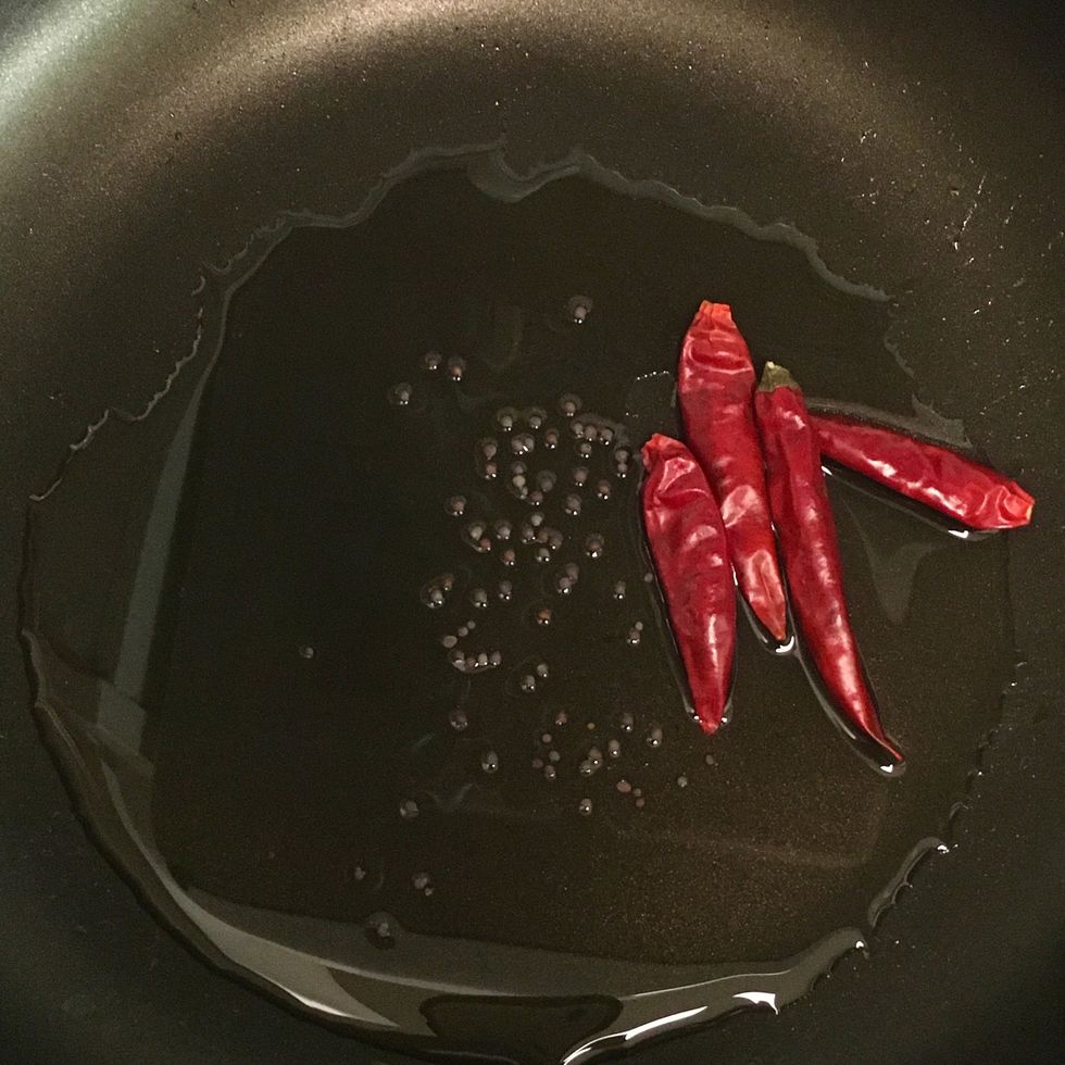 In a shallow pan over medium heat, add canola oil. As the oil heats up, add black mustard seeds and Japanese chili pods.