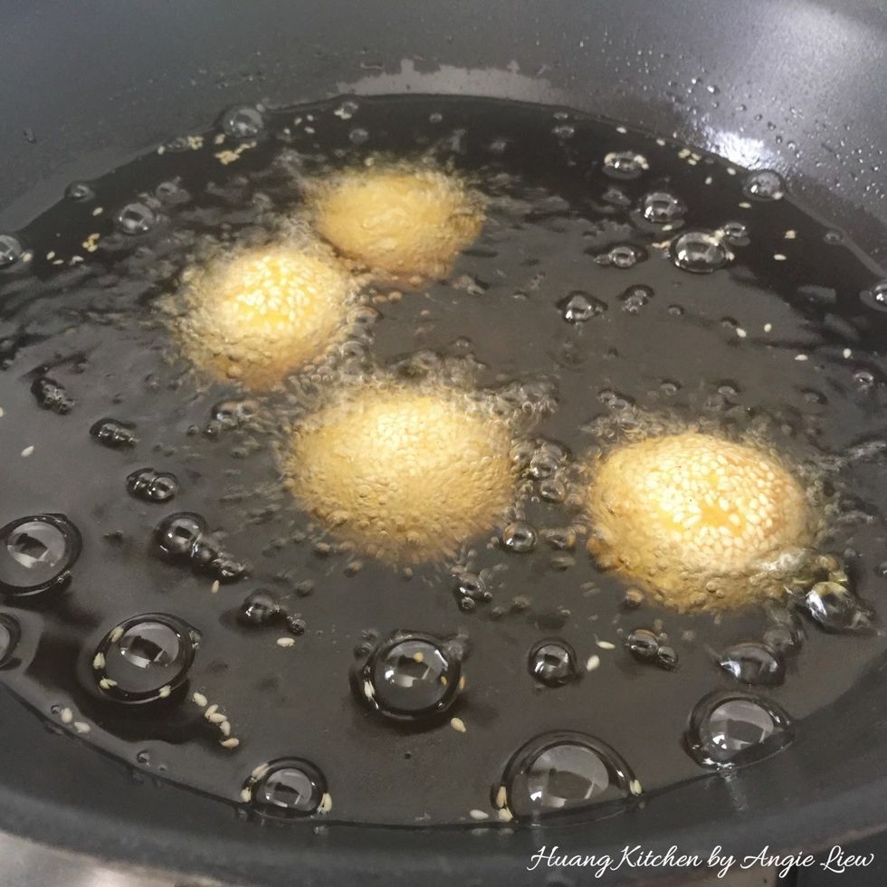 In batches, add in sesame cookie balls into the hot oil. Then bring the temperature to medium low and fry the dough for about 10 minutes or until the balls crack and are about golden brown in colour.