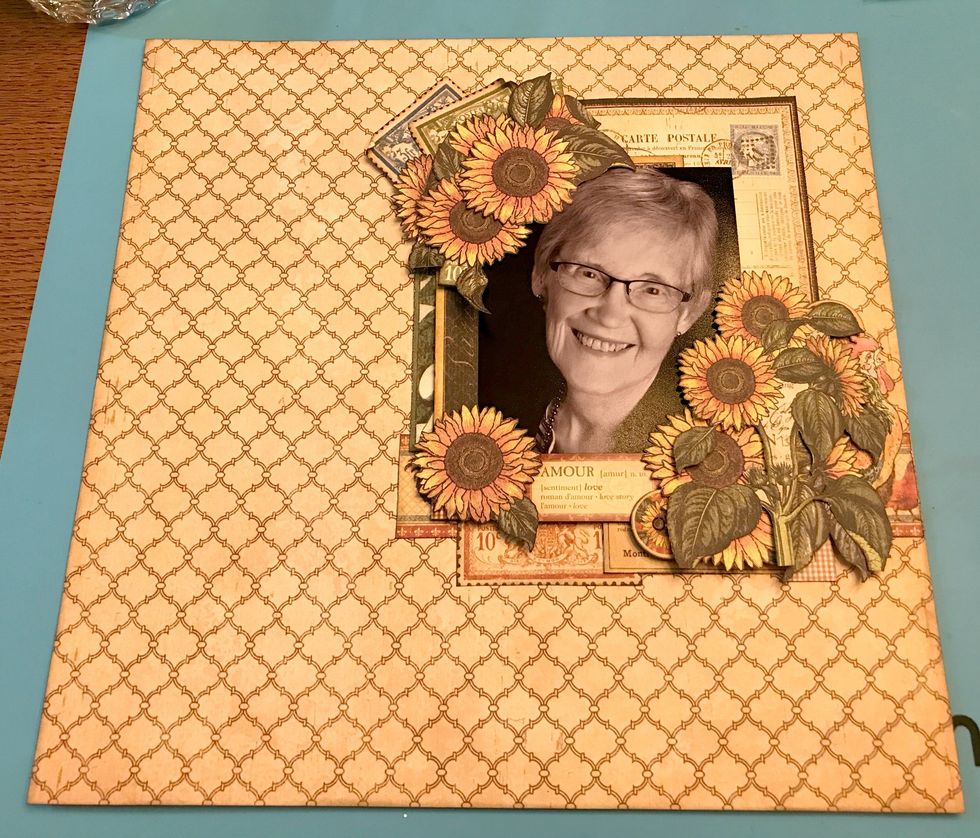 In the bottom left hand corner of the photo, foam square one sunflower. Adhere a photo corner underneath the sunflower. Adhere a second photo corner onto the cream with black writing card.