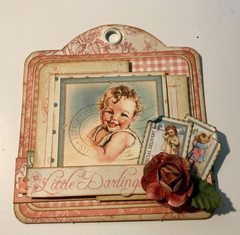 In the bottom right hand corner of the baby image, adhere a flower and two postage stamps. Roll one corner down on each postage stamp.