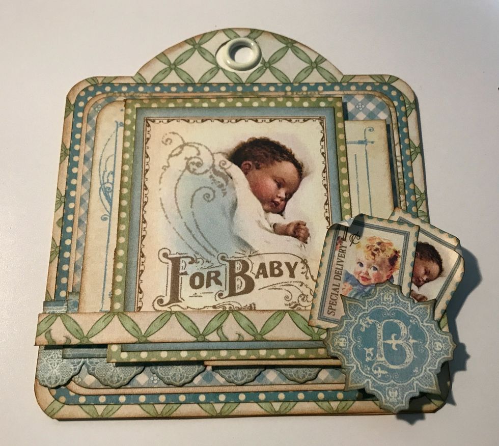 In the bottom right hand corner of the baby image, adhere the B image and two postage stamps. Roll one corner down on each postage stamp.
