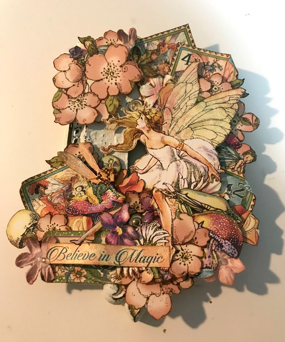 In the top left corner, adhere the remaining flowers. Use foam squares as desired. On the bottom left side, adhere the believe in magic sentiment.
