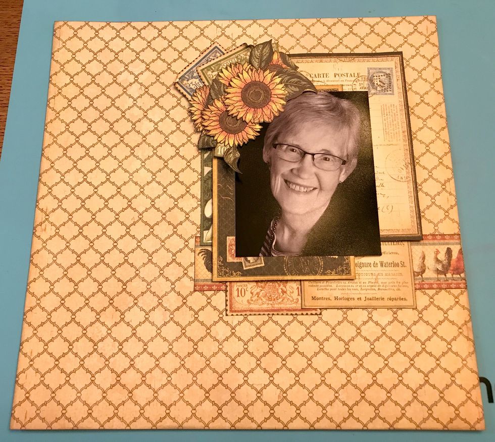In the top left hand corner of the photo, use foam squares and adhesive to adhere five sunflowers, two post 10cents and two stamps.