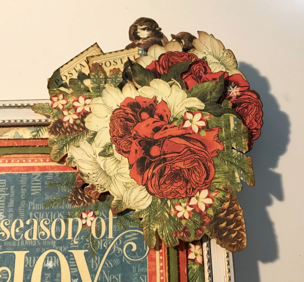 In the top right hand corner of the frame, adhere the floral bunch, the two birds, the two red roses with white flower and two stamps. Roll one of the corners down on each stamp.