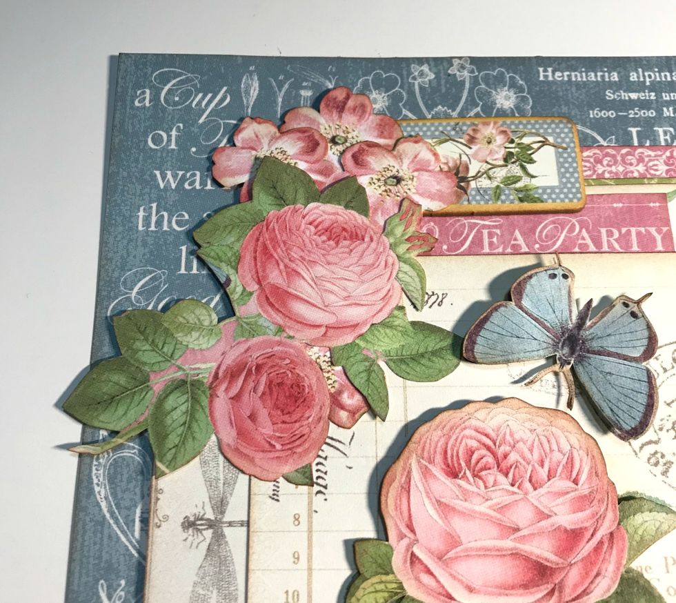 In top left corner of rose/butterfly card, adhere rose bunch. Adhere a 1 pink flower underneath the 2 roses. Adhere 3 pink flowers to right of the rose. Adhere the rose tag to right of pink flowers.