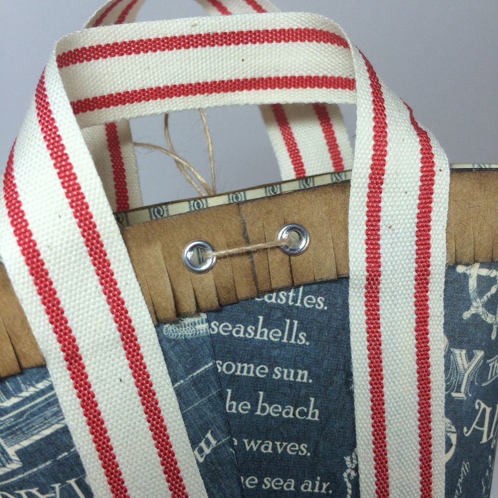 Insert silver eyelets and set with an eyelet setting tool. (I use the Crop-a-dile.) Thread an 18 inch piece of thin twine through the back two holes and pull the tails through the front hole.