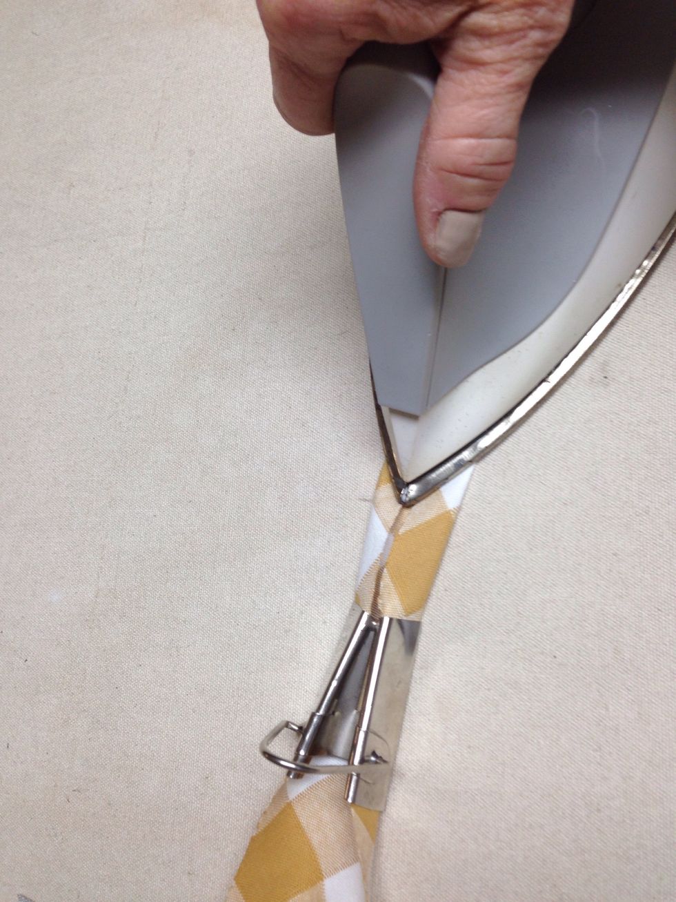 Iron the fabric as you pull it through the tape maker. http://www.patemeadows.com/Using-Bias-Tape-Makers_ep_62.html