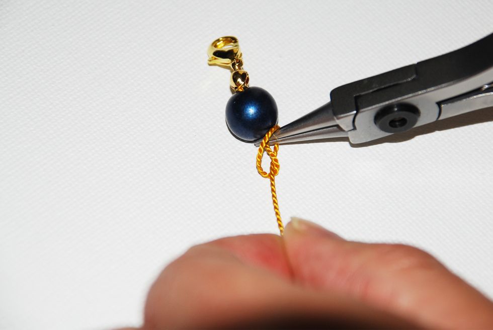 Keep holding the thread with your round nose pliers and start pulling on the long thread, tightening the loop over the tip of the pliers - until it turns into a knot.