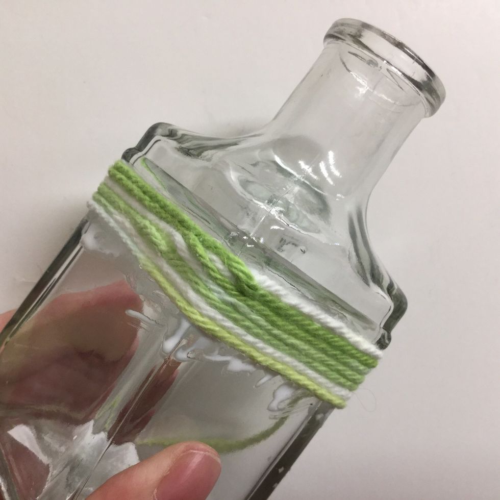 Keep wrapping the yarn around the bottle, covering the starting end. Continue applying bands of glue and wrapping the yarn until you reach the bottom. Trim the yarn and press the end firmly in place.