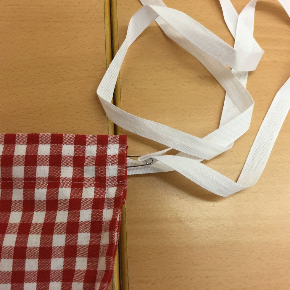 Klipp av ett bomullsband 2 m l\u00e5ngt. Tr\u00e5 det i kanalen med hj\u00e4lp av en s\u00e4kerhetsn\u00e5l 2 varv. Knyt ihop.