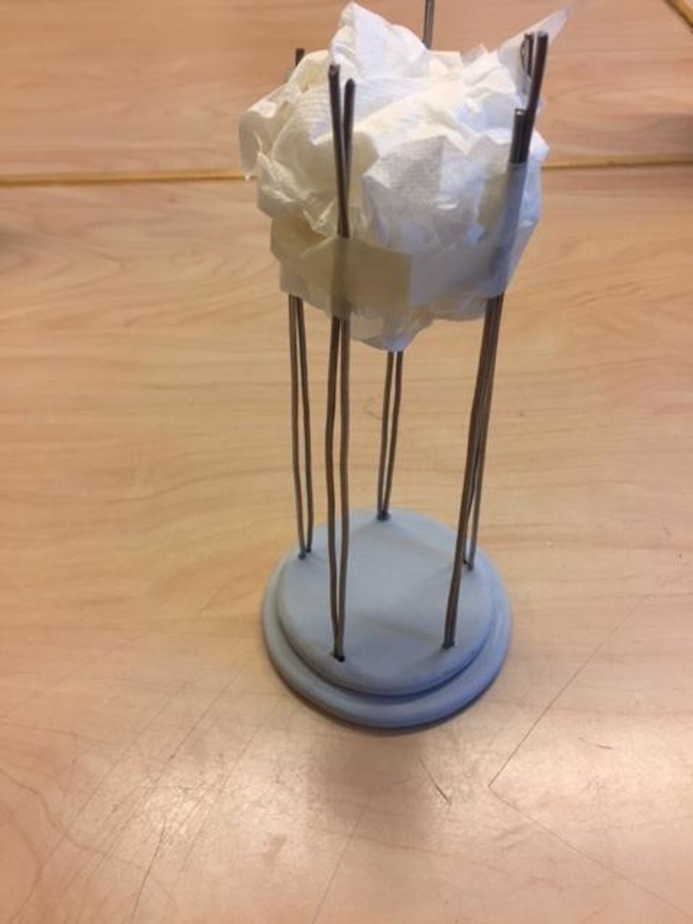 Knyckla ihop en pappershandduk till en boll. Tryck sedan ner bollen av papper mellan metallpinnarna h\u00f6gst upp. Ta maskeringstejp och  tejpa runt om s\u00e5 att pinnarna h\u00e5lls raka n\u00e4r de torkar.