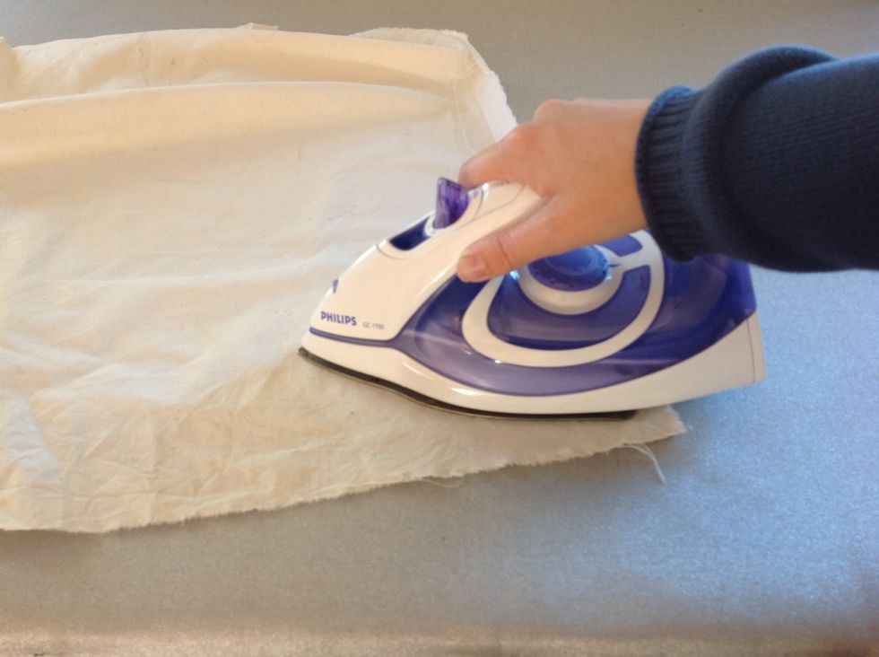 L\u00e4gg \u00f6ver skyddsduken. Var f\u00f6rsiktig s\u00e5 att vliesofixbiten inte flyttar p\u00e5 sig. Stryk med strykj\u00e4rnet p\u00e5 tv\u00e5 prickar.