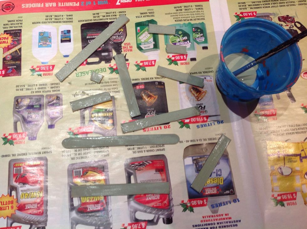 Lay down newspaper and paint one side of all of the pop sticks, including the one you set aside. Once dry, paint the other side.