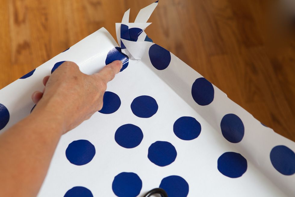 Lay gift wrap on table and use fingers to crease the paper all along the edges to get a perfect fit. The crease will become the cutting line.