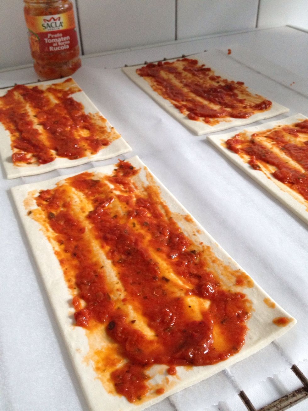 Lay puff pastry sheets out on baking paper (let them thaw if frozen) and spread the red pesto.
