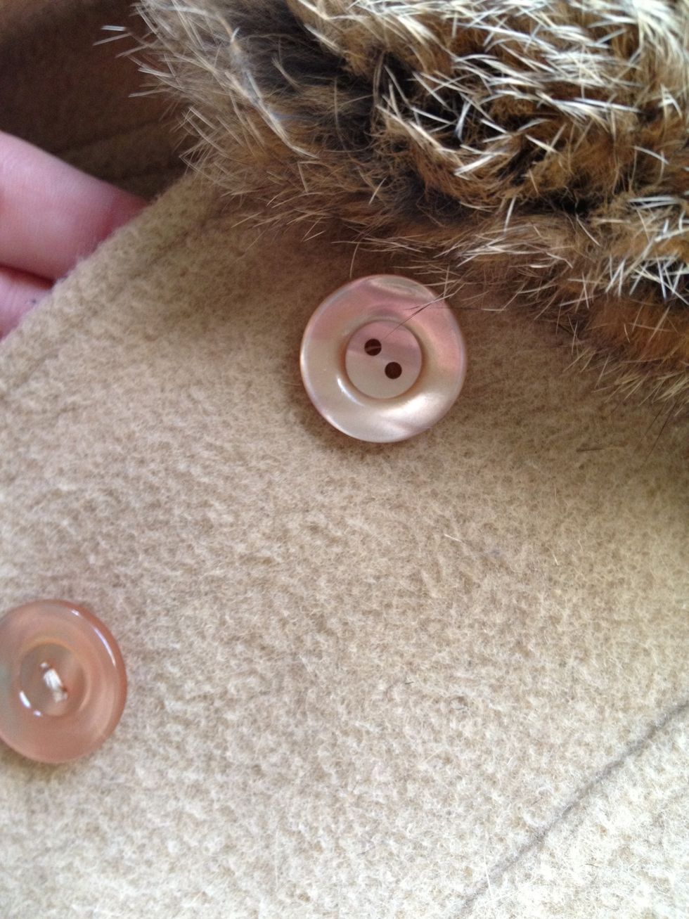 Lay the coat or material flat, make sure to match up the button holes to the remaining thread or holes from where it was originally sewn on.