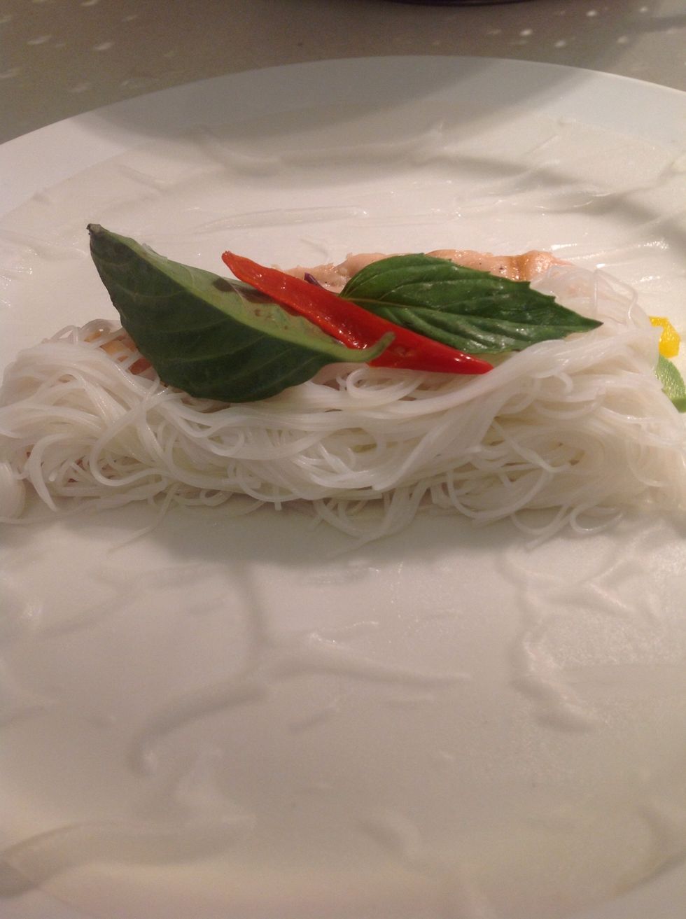 Lay the paper on a plate. Place the ingredients on the middle of it like this: a strip of salmon, a line of vermicelli, a pickled pepper or two, some avocado and peppers and loquat, a few leaves.