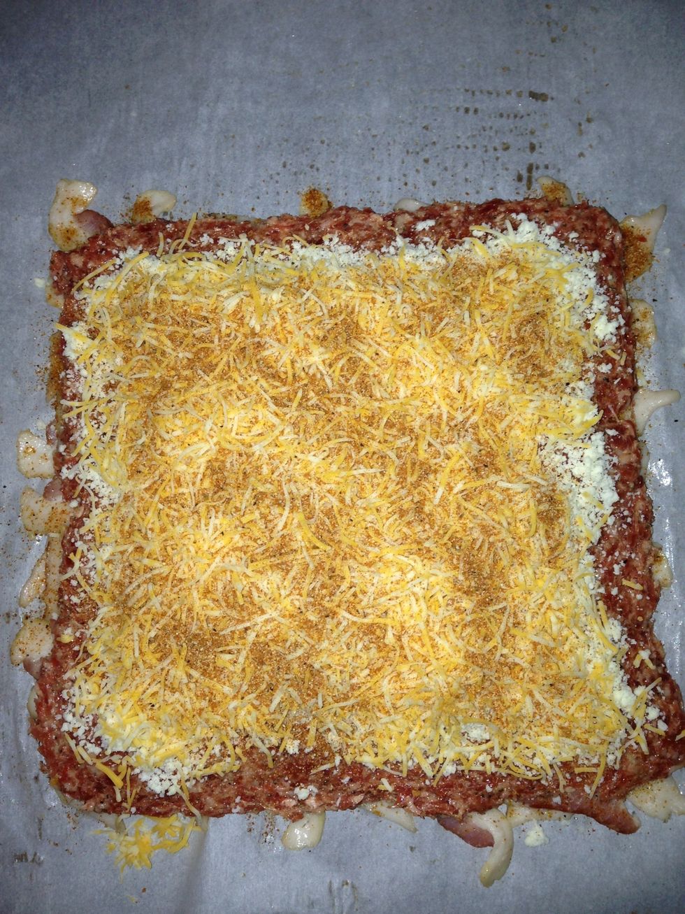 Lay the sausage patty over the bacon weave. Add cheese.  This is a layer of crumbled asiago and then some shredded Colby jack.  Sprinkle more of the rub over the cheese.