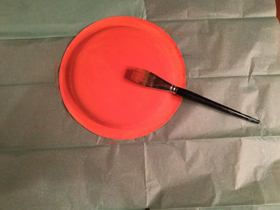 Lay your paper plate over a protective surface and paint it orange.