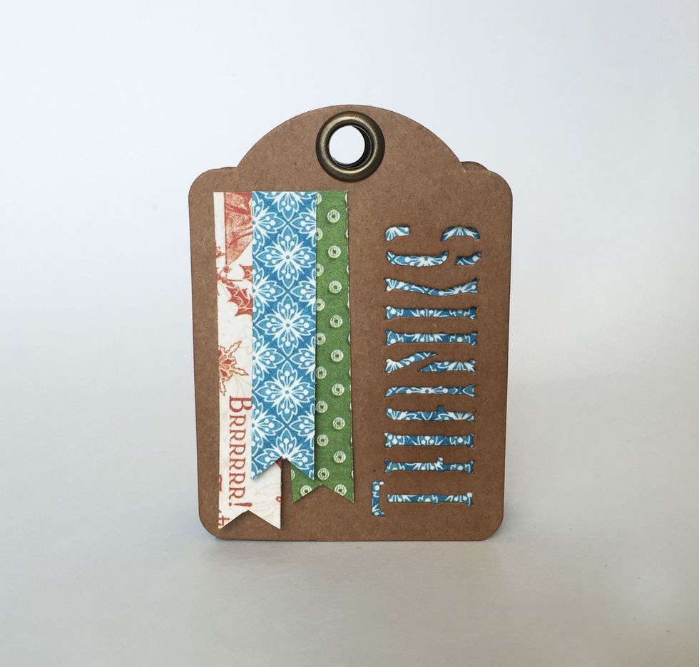 Layer and glue the pennants to the left of the \u2018Thanks\u2019 cutout on the tag, as pictured or as desired.