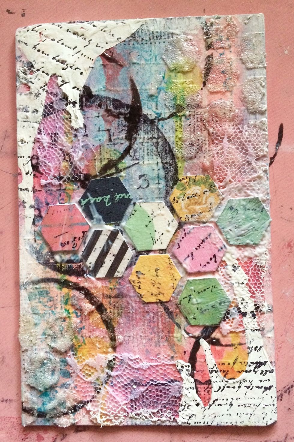 Layer your hexagons across the middle of your board. Mod Podge them down. Once it is dry, add a script stamp across your project and over your white gesso.