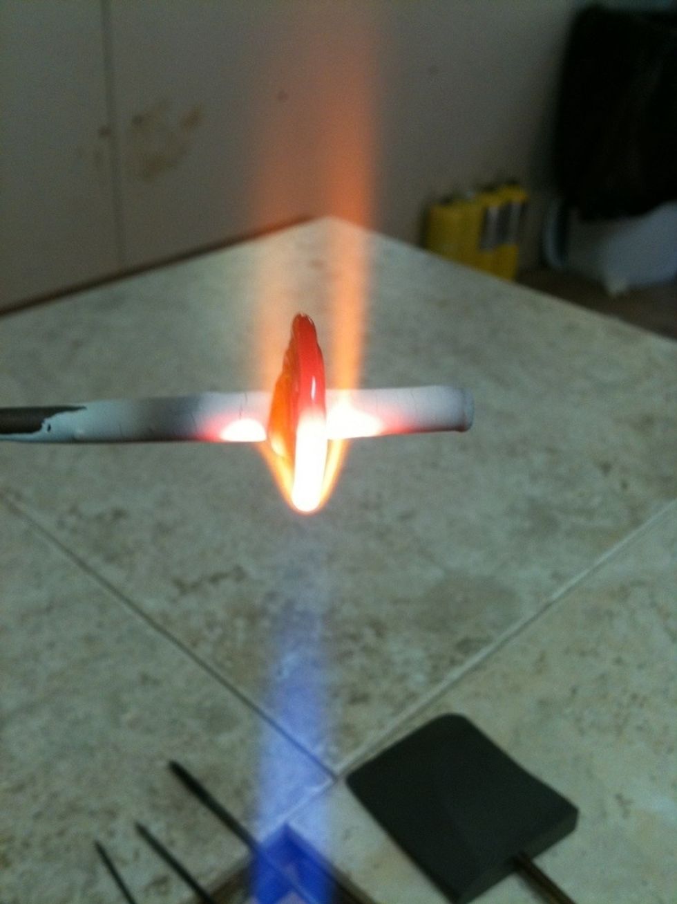 Laying on the first twistie. I will use one of the pokers to reshape the core black bead and move the twistie. The mandrel is constantly turned by hand throughout the process to keep the bead round.