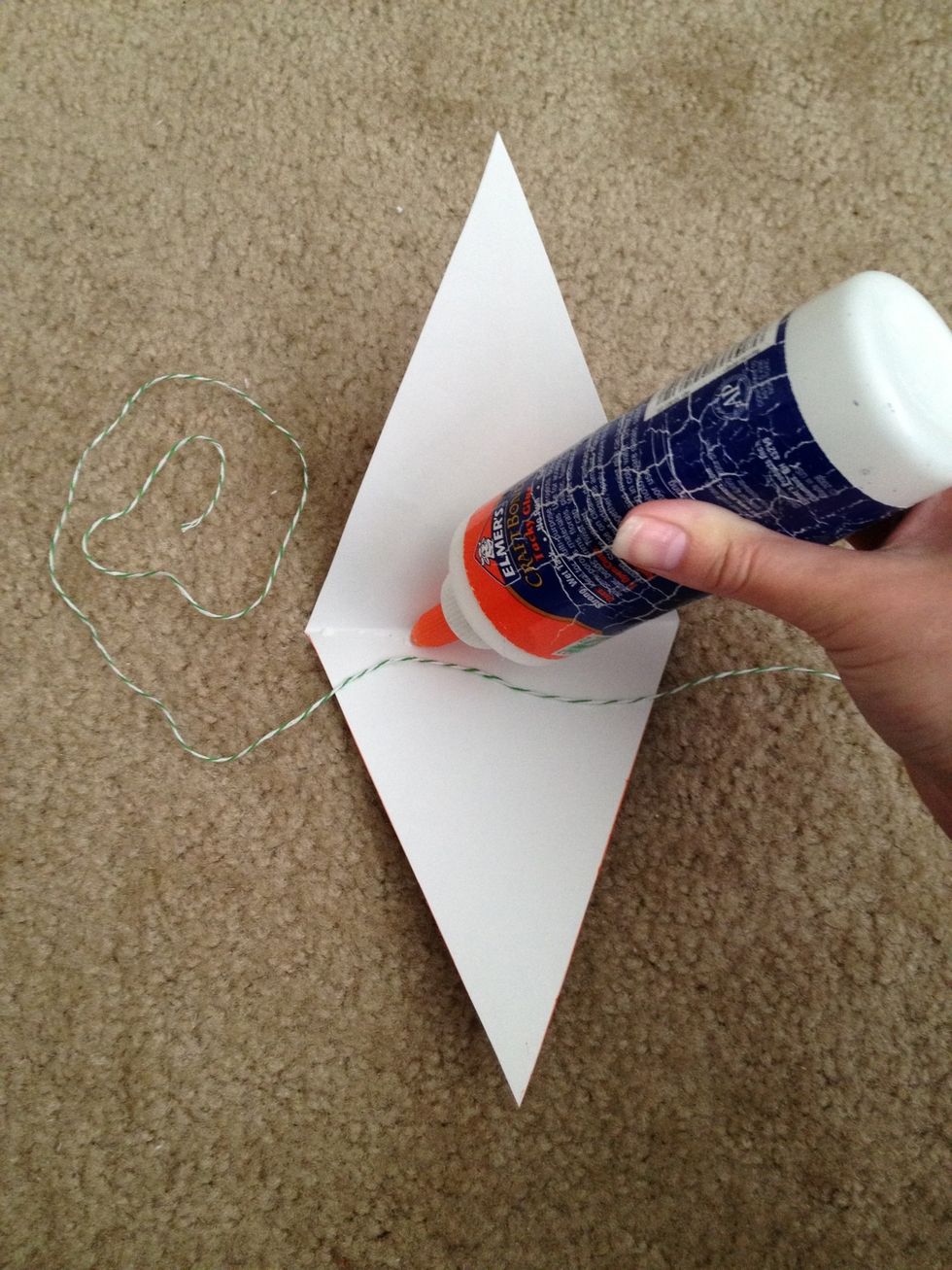 Leave extra string to the left of the triangle for easier hanging. Open the triangle and place glue along the crease. Place the string directly on top of the glue and string and fold the triangle.