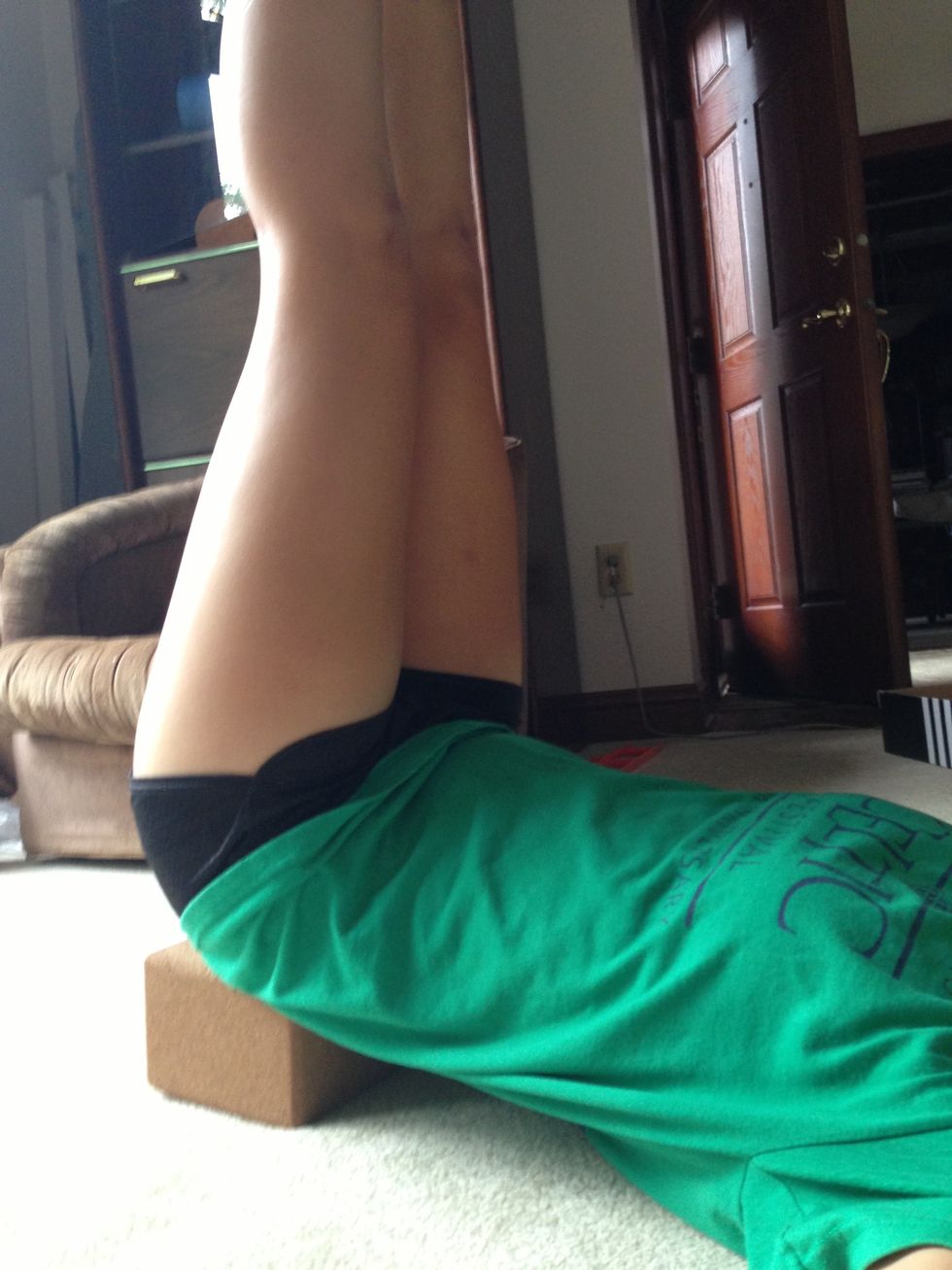 Lie down against a wall or any flat perpendicular surface or prop your tush up with a yoga block to prop your legs straight up in the air