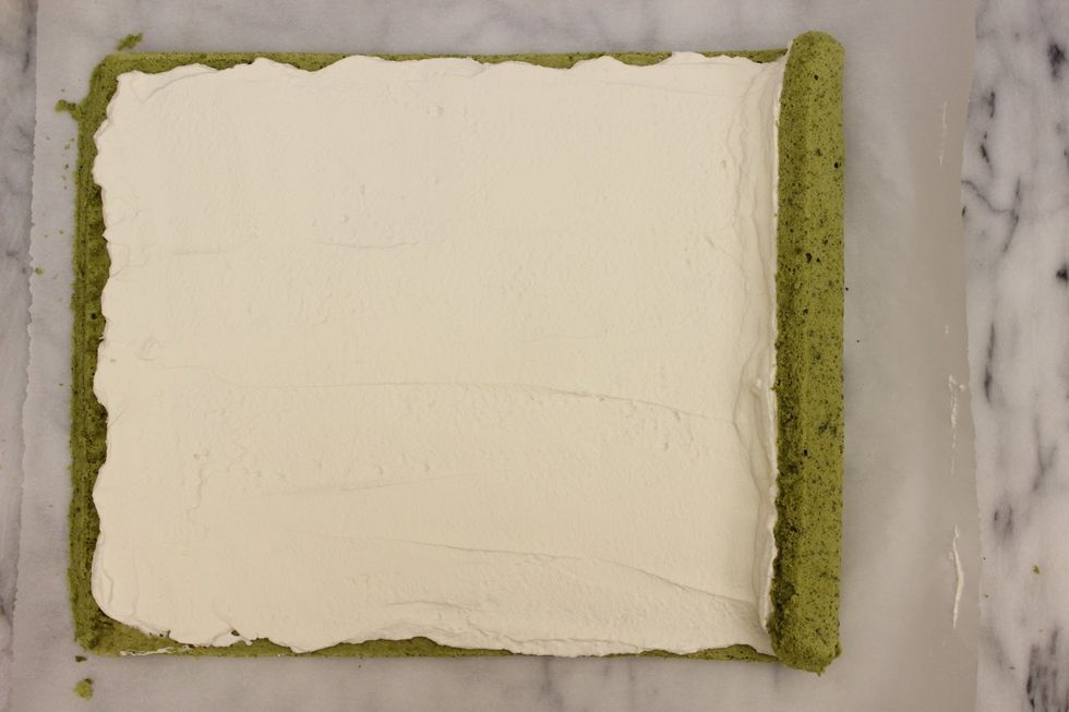 Lift the parchment paper on the right side to start rolling the cake.