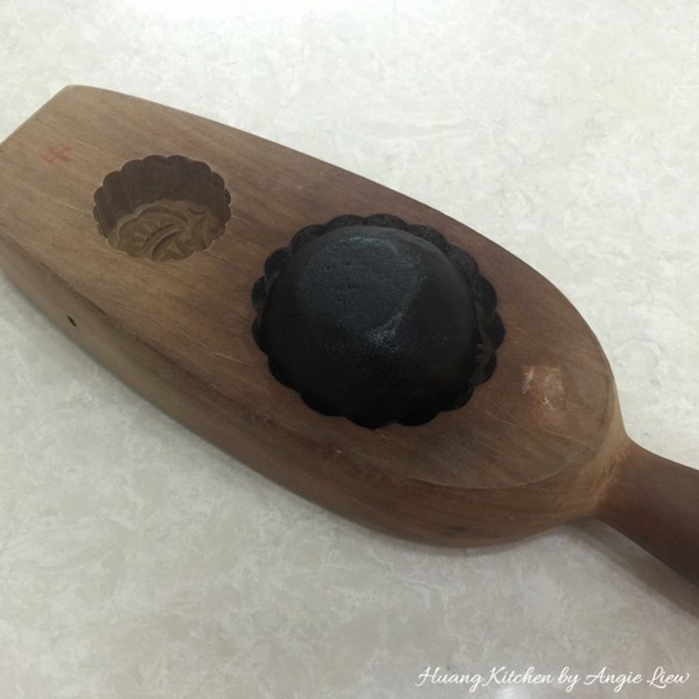 Lightly dust the wrapped dough and place it into the floured mooncake mould. Using your fingertips, lightly press the dough to imprint the shape of the mould.