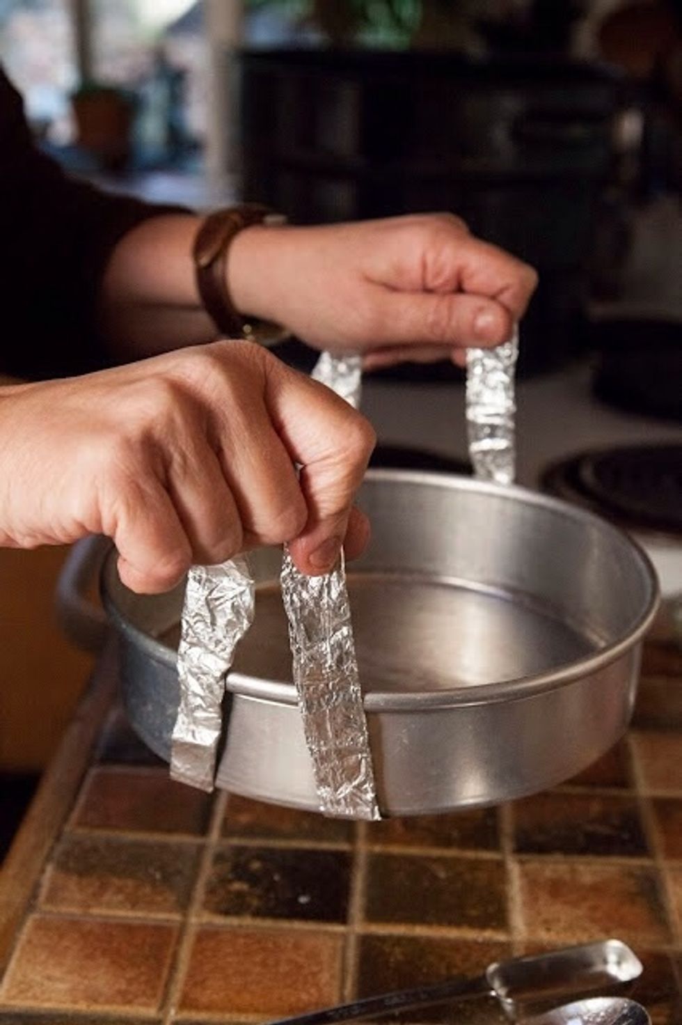 Lightly grease an 8 inch cake pan. I make thin little straps of folded tin foil and loop them under the bottom of the pan to make it easier to lower it into the pot. Like this.