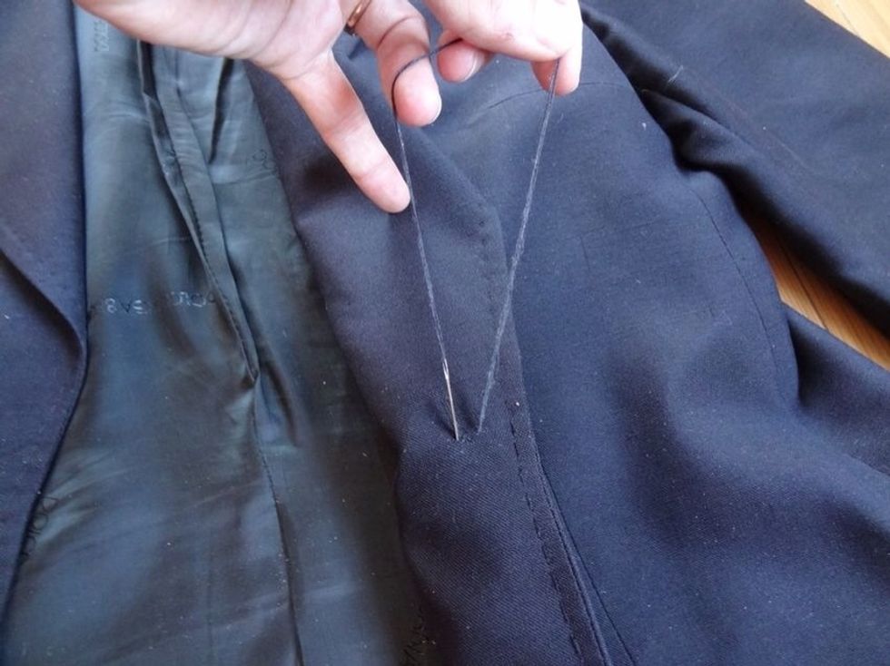 Line up your button to the holes left by the old button. From the underside of the coat, push the needle through the fabric, pull it tight, and loop it through the round hook of the button.