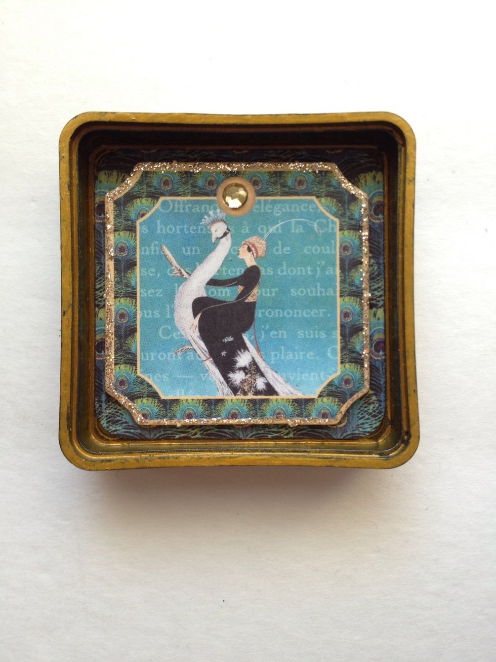 Locate the chipboard piece shown in the photo. Add some Stickles in Platinum around the border, then adhere a large crystal. Adhere to the inside of your lid.